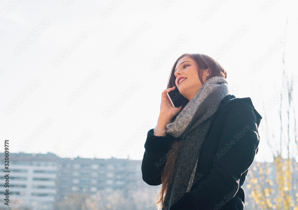 Attractive young girl with long hair and winter clothes speaks on the phone on the street.