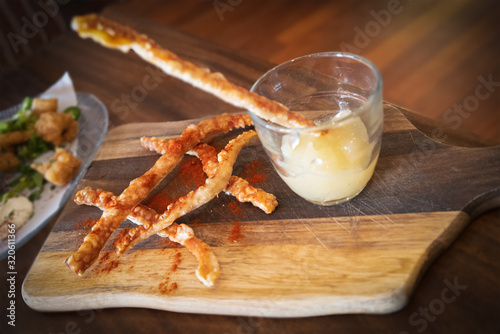 Tasty pork crackling strips and an apple sauce dip in a glass on a wooden board served as a snack or appetiser