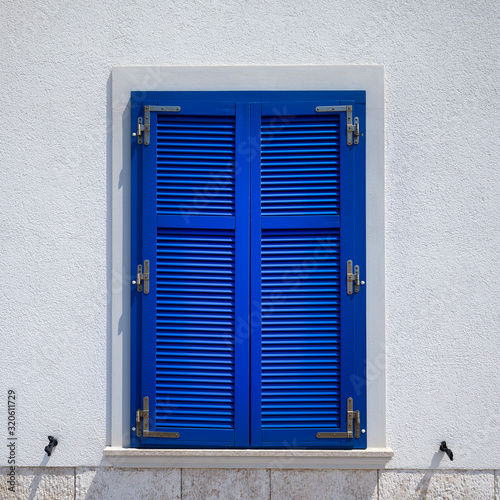 Stone house with window with shutters. A bunch of wooden window shutters pattern on white stone wall. Naked worn wooden and plain painted shutters. Hipster loft wallpaper.