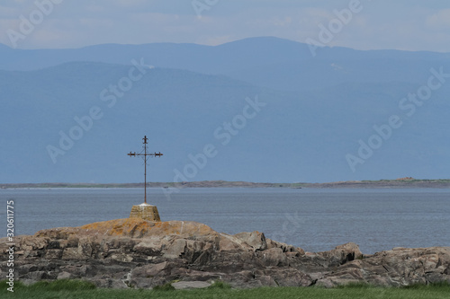 Cross on a rock on the shore of Saint Lawrence river and view on the mountains