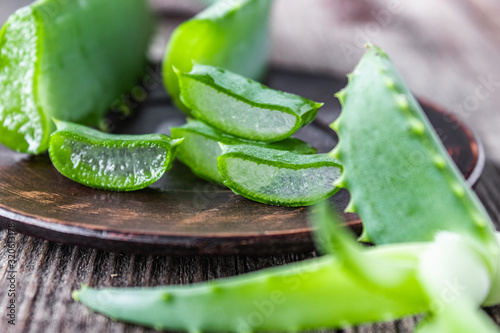 Fresh aloe vera leaves and slices of aloe vera in a bowl on a wooden background.