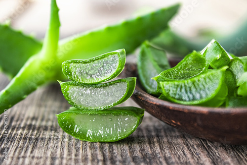 Fresh aloe vera leaves and slices of aloe vera in a spoon on a wooden background.