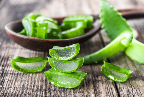 Fresh aloe vera leaves and slices of aloe vera in a spoon on a wooden background.