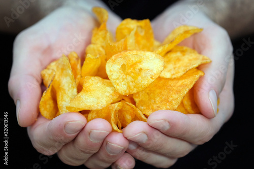 The guy holds potato chips in his hands. Hands with chips close-up. Harmful junk food for health. Potato snacks for beer.