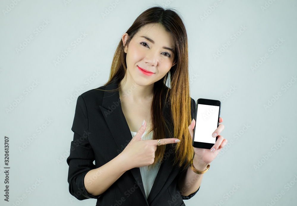 Portrait of stressed asian business woman showing and pointing to empty white mobile screen. Caucasian female model isolated on white background. selective focus