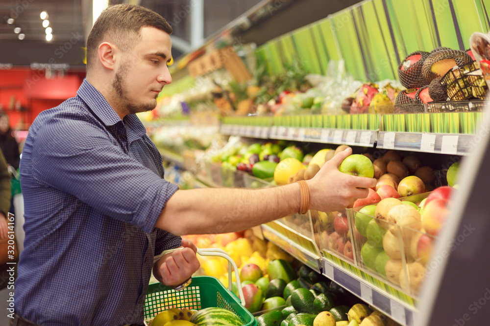 Man in a supermarket at the shelf for fruits shopping for groceries, he is checking out the apples. Man in a supermarket at the shelf for fruits shopping for groceries, he is checking out the apples.