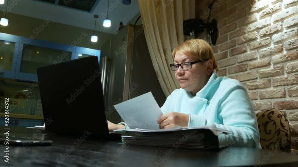 elderly woman working at home with the documents using laptop.
