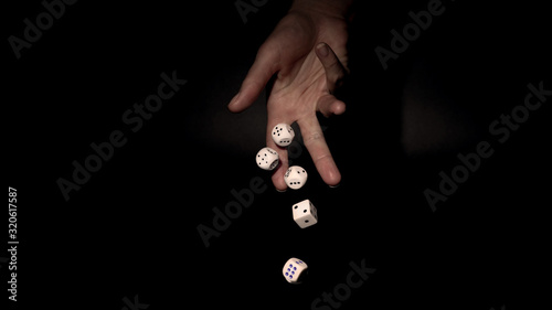 Hand throwing gambling dice on  table, black background 