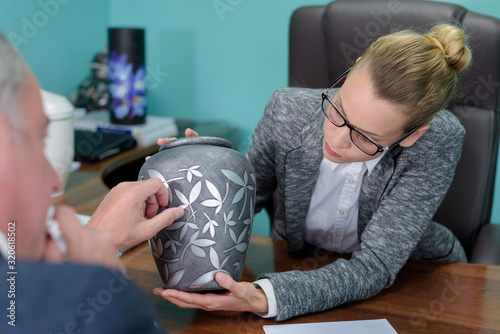 Valokuva female funeral director showing urn to bereaved man
