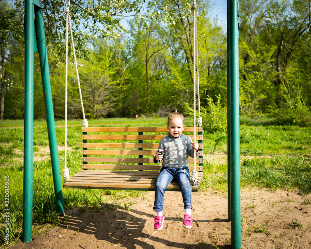Child eating ice cream in a black waffle cone sitting on a swing Child eating ice cream in a black waffle cone sitting on a swing