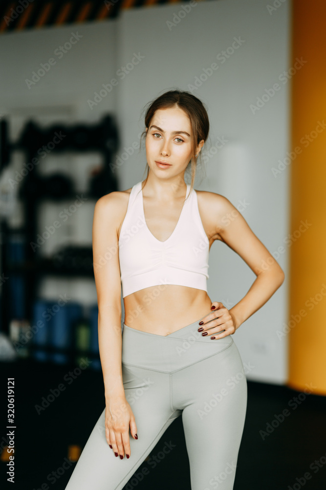Stands after a workout with a watch. Portrait of a sports girl in the gym. Beautiful white girl for advertising.