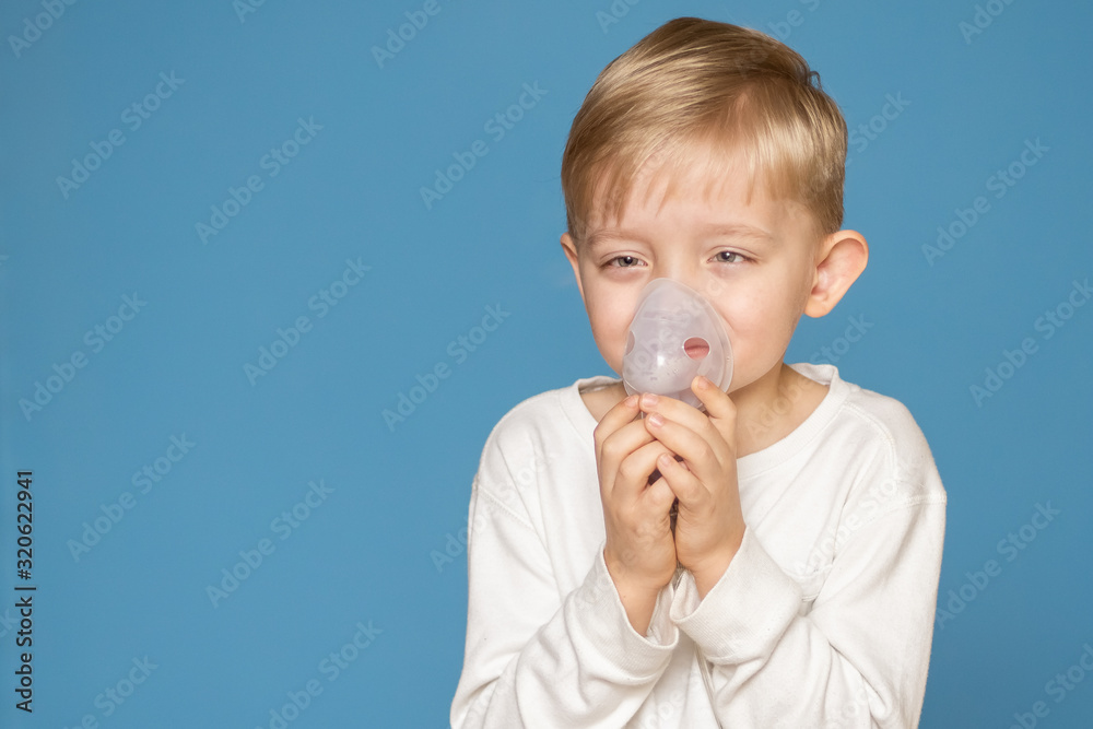 A strabismus boy doing inhalation with a nebulizer on a blue background. A strabismus boy doing inhalation with a nebulizer on a blue background.