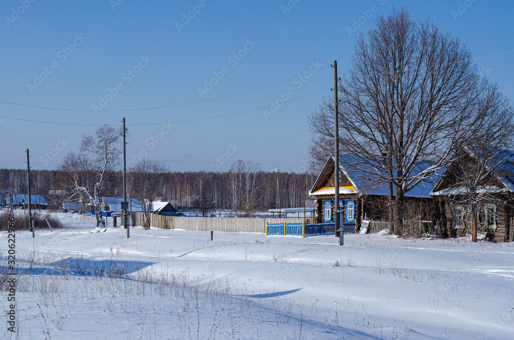 Winter landscape on a Sunny day. View of the Russian village in the snow. Authentic Wooden houses and footprints in the snow.