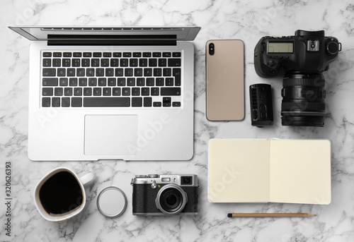 Flat lay composition with laptop, cameras and smartphone on white marble table. Designer's workplace
