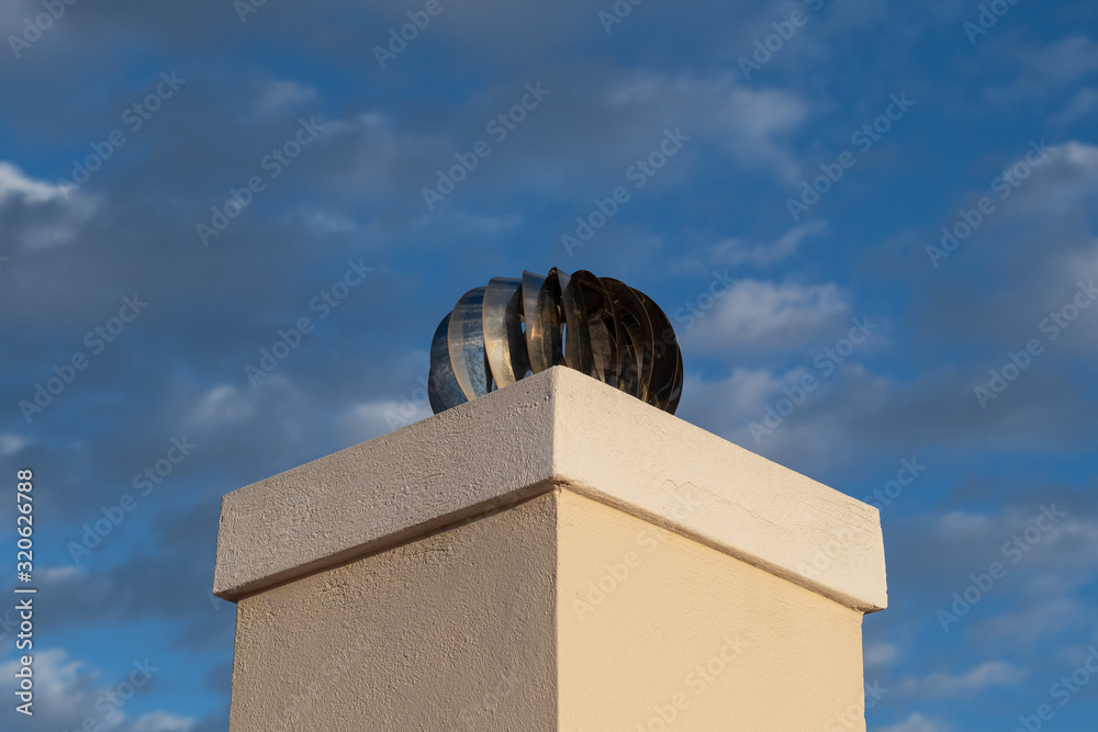 Fototapeta premium Spinning stainless steel cowl cap on top of chimney with blue sky and clouds in background