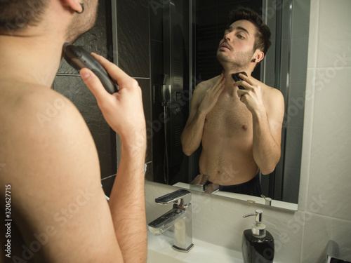 Portrait of handsome caucasian teenager reflection in from of the mirror, shaving with a shaver