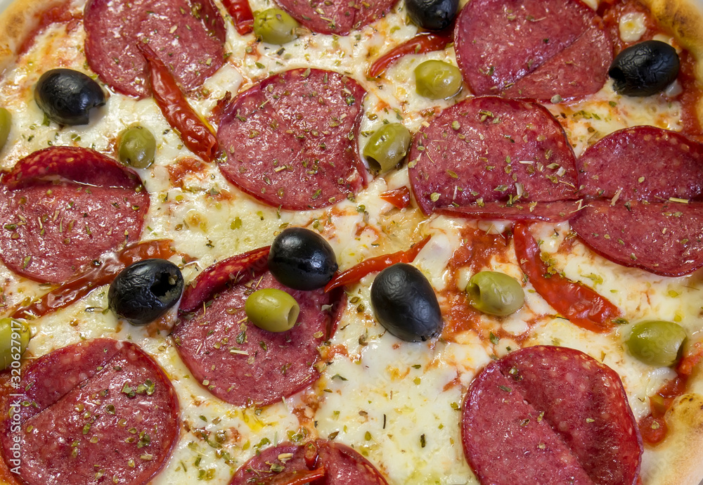 Spicy devil's pizza with salami slices and red pepper pods pepperoni and black olives.