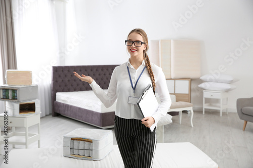 Young saleswoman with clipboard in mattress store