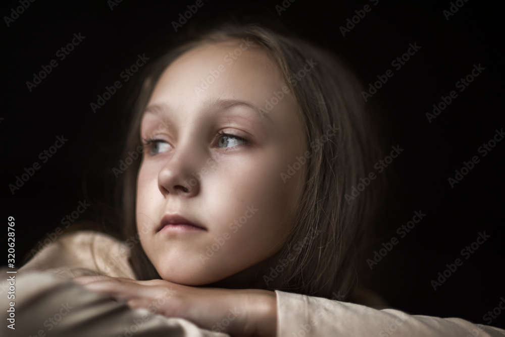Dramatic portrait of a pensive girl against a dark background. Dramatic portrait of a pensive girl against a dark background.