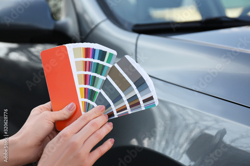 Woman with palette samples choosing color for painting car, closeup