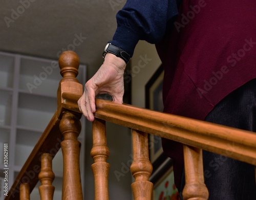 Senior person is climbing stairs while holding hand rail for support