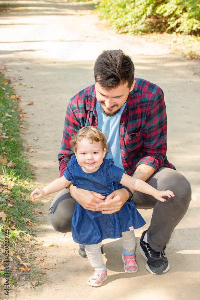 Fototapeta premium Laughing curly girl runs away from dad park. Young Caucasian European man plays with his daughter outdoor