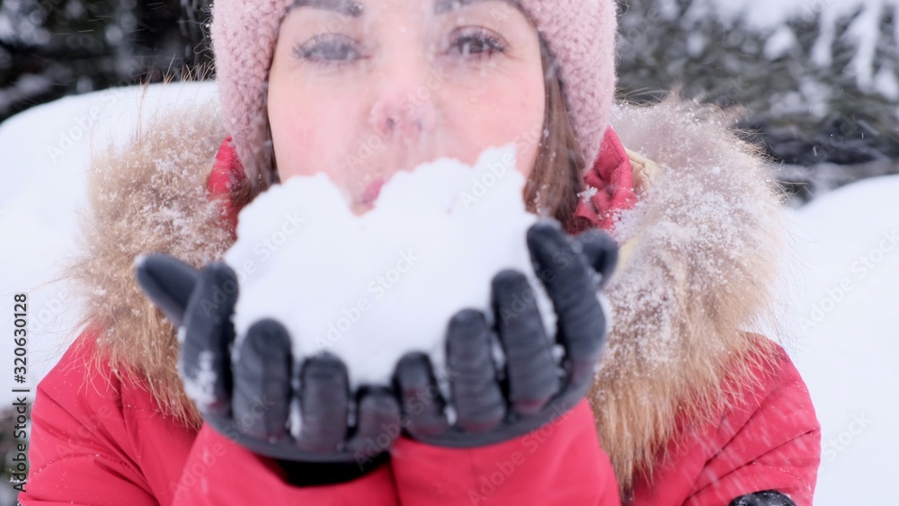 Smiling young woman in red jacket throwing snow in the air on a sunny winter day. Woman blows snow from her hands Smiling young woman in red jacket throwing snow in the air on a sunny winter day. Woman blows snow from her hands