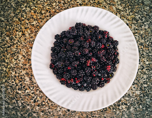 White plate full of blackberry on the table. Stylish food background