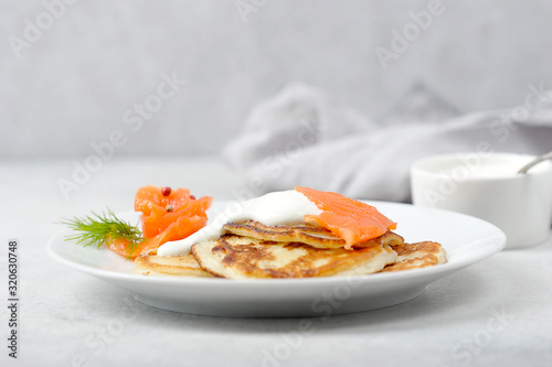 Fritters with salted salmon and sour cream.  A cup of sour cream next to a plate.  Serving concept.  Light background.  Close-up.