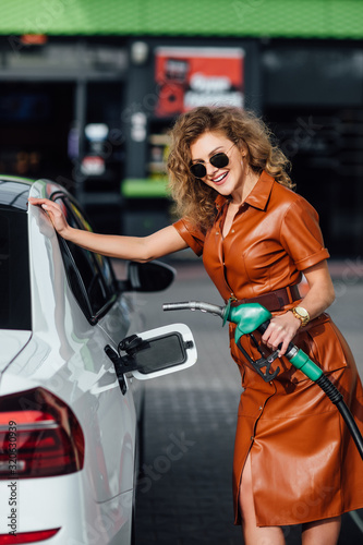 Attractive, young woman refueling her car in a gas station, checking the amount of gas.