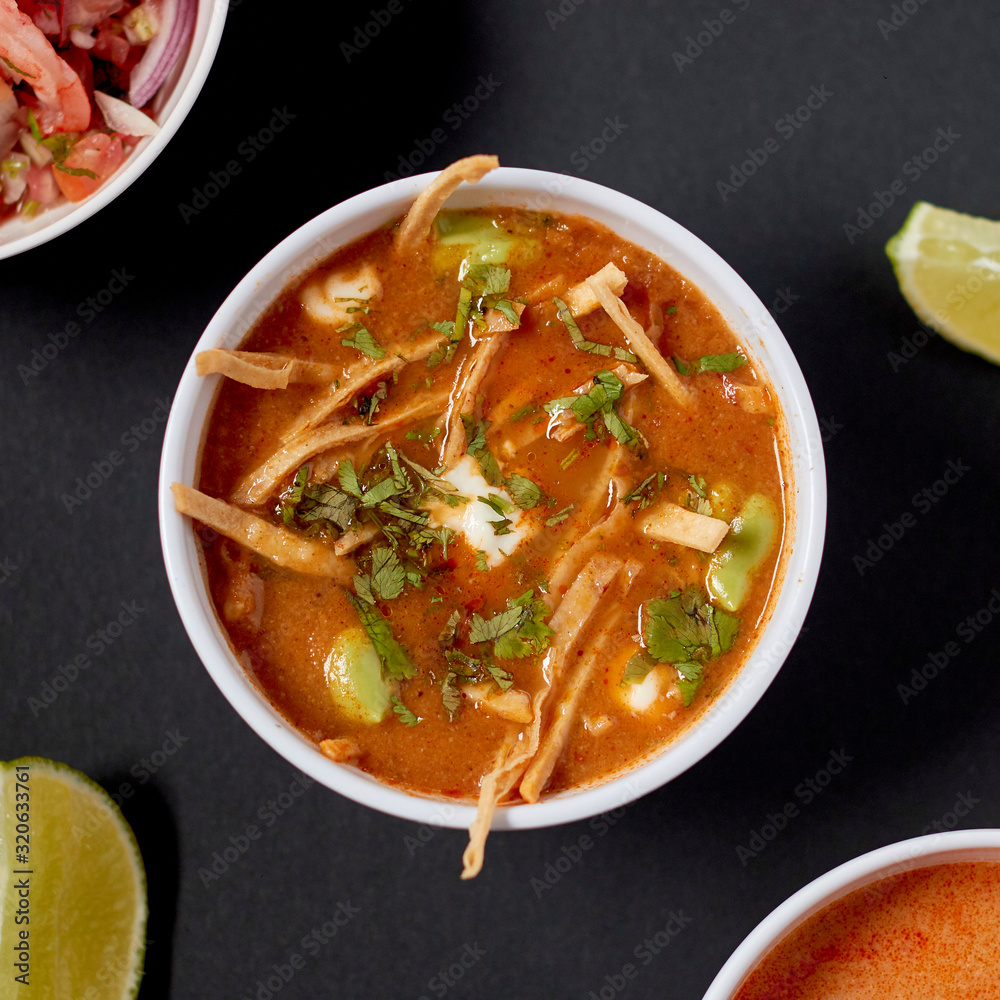From above yummy nutrient tomato soup with sour cream and aromatic green herbs in white ceramic bowl on gray table beside variety other dishes From above yummy nutrient tomato soup with sour cream and aromatic green herbs in white ceramic bowl on gray table beside variety other dishes