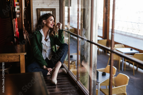 From above of pensive trendy woman sitting with crossed legs and looking through window of modern cafe photo