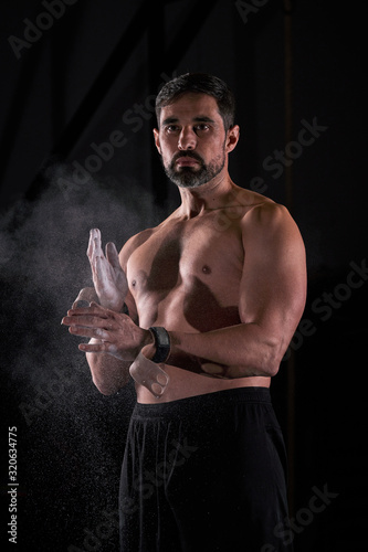 Strong man preparing strength exercises in the gym with magnesium in his hands. Young athlete practicing multidisciplinary training photo