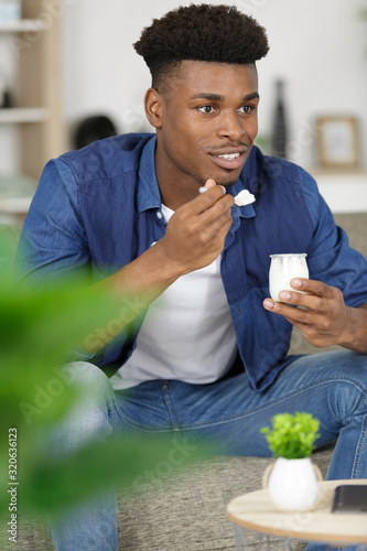 man sat on the sofa eatning a yoghurt photo