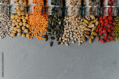 Horizontal shot of various multicolored grains spilled from glass bottles, isolated over grey texture background. Food with healthy benefits photo