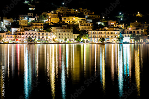 Fotografia Poros, Greece at night hillside waterfront city with lights reflecting in the wa