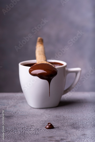 from the wooden spoon, smeared with melted chocolate, drops of chocolate fall on the gray worktop photo