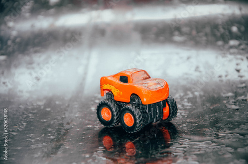 Red little toy car with big wheels in macro. Toy monster car. Blurred background CopySpace Copy Space Wet background, raindrops © Arthur Shevtsov