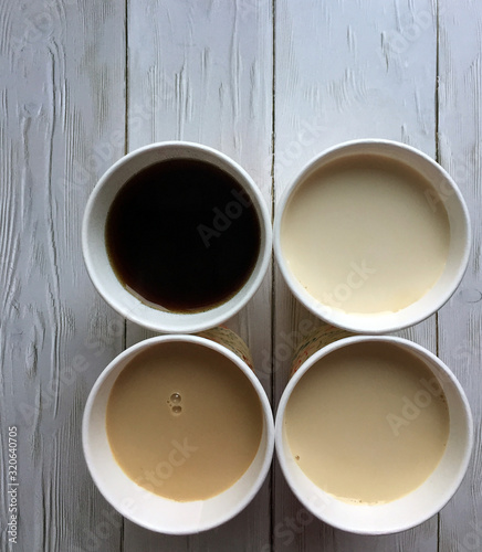 Four paper cups of coffee with milk on a wooden white background close up with space for copying. Flat lay