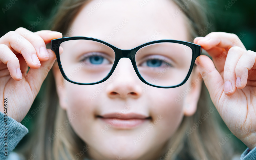 Closeup portrait of little girl with myopia correction glasses. Girl is holding her eyeglasses right in front of camera with two hands - focus on glasses - shallow depth of field Closeup portrait of little girl with myopia correction glasses. Girl is holding her eyeglasses right in front of camera with two hands - focus on glasses - shallow depth of field