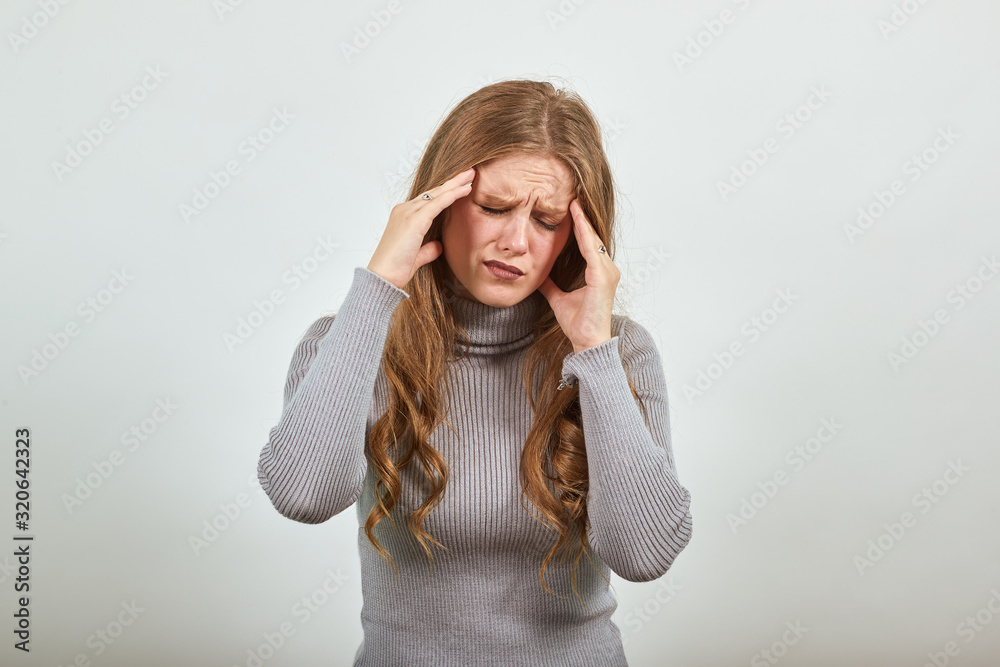 a young beautiful red haired woman in gray sweater is suffering from headache she is holding hand on head