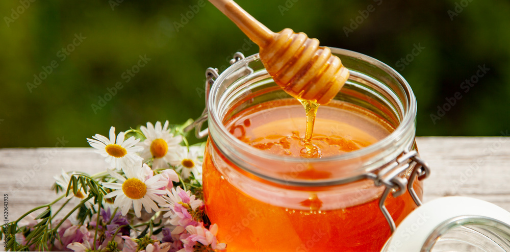 Honey in glass jar with bee flying and flowers on a wooden floor. Honey in glass jar with bee flying and flowers on a wooden floor.
