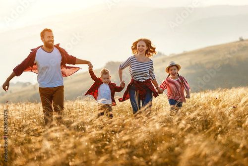Happy family: mother, father, children son and daughter runing and jumping on sunset.