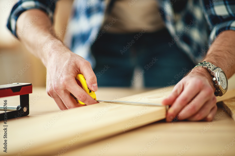 .    carpenter's hands with tape measure and pencil measure wooden Board