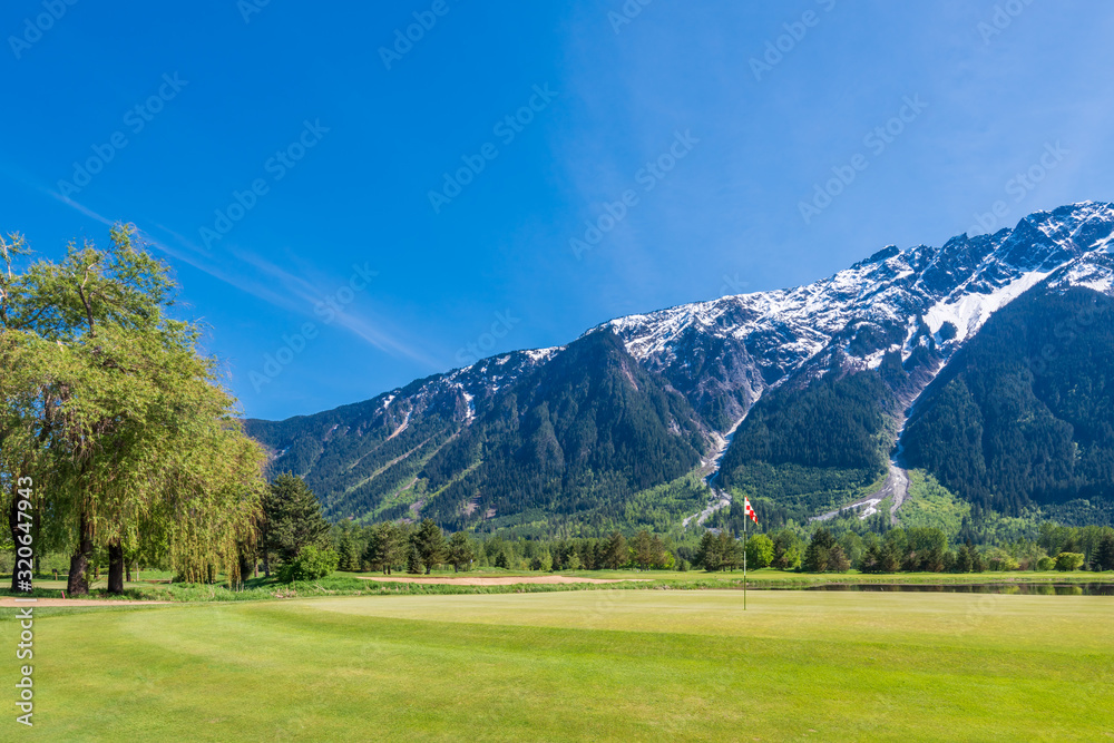 Golf course with flag, gorgeous pond and fantastic snow mountain view.