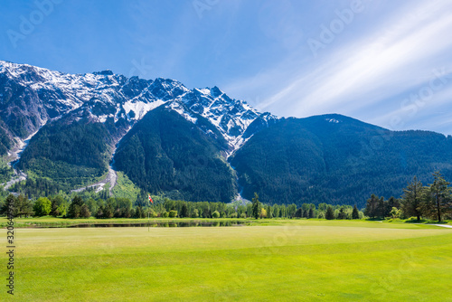 Golf course with flag, gorgeous pond and fantastic snow mountain view.