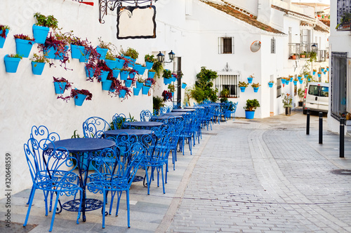Fototapeta Naklejka Na Ścianę i Meble -  Mijas Pueblo Blanco, charming small village, picturesque empty street in old town with bright blue tables chairs of local cafe, flower pots hanging on white washed houses walls, Costa del Sol, Spain