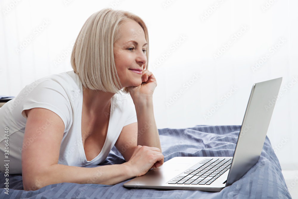 Smiling attractive woman lying on bed using laptop communicating online at home, happy girl typing on computer, enjoying internet shopping or chatting in social networks in bedroom. Smiling attractive woman lying on bed using laptop communicating online at home, happy girl typing on computer, enjoying internet shopping or chatting in social networks in bedroom.