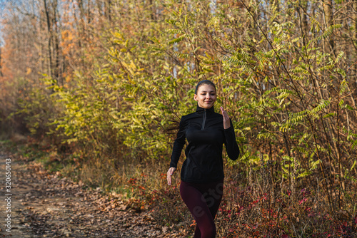 Attractive brunette girl in dark sportswear running along the dirt road among the forest © Vasya