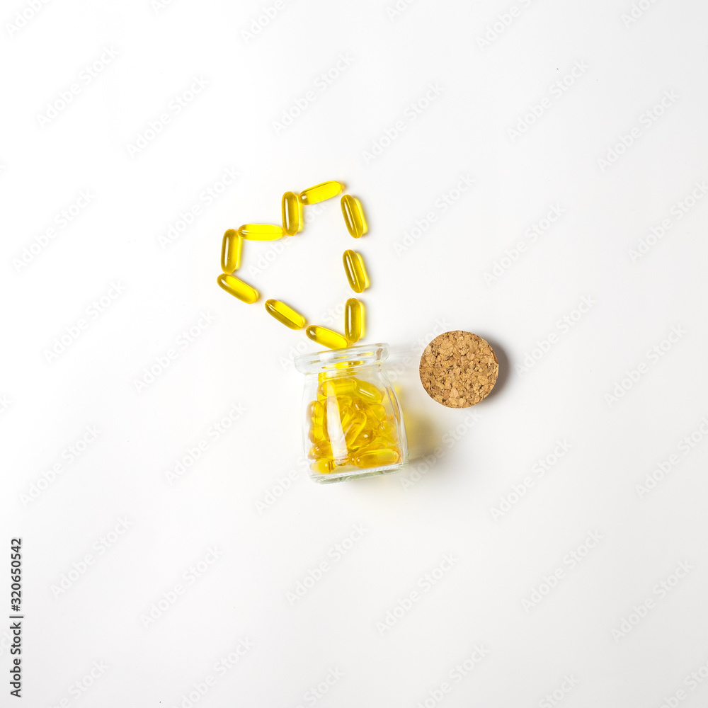 Glass vial with yellow vitamins tablets, fish oil, Omega Vitamin E. A small retro jar with a cork, lies with scattered pills in shape of heart on a white background. Flat lay with a copy space.